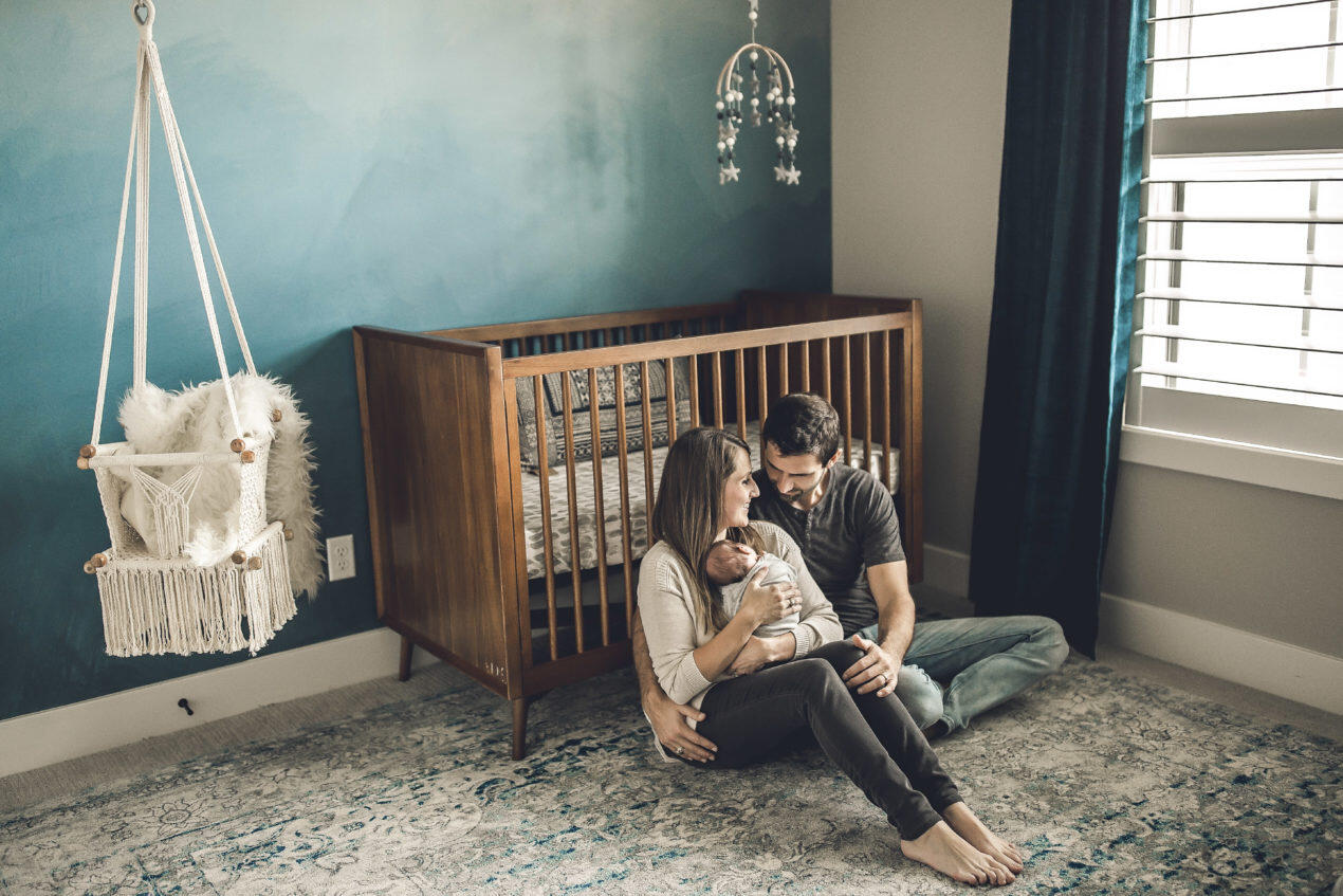 Mom, Dad, and Newborn sitting in front of crib next to ombre blue mural